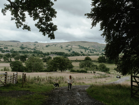 Helen walks in the landscape with her dog floss, rolling hillside reaches out behind her