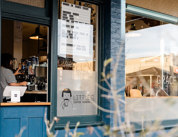 Barista at coffee machine seen through window of blue cafe