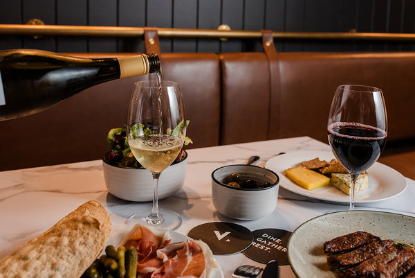 Pouring glass of wine among spread of dishes on restaurant table