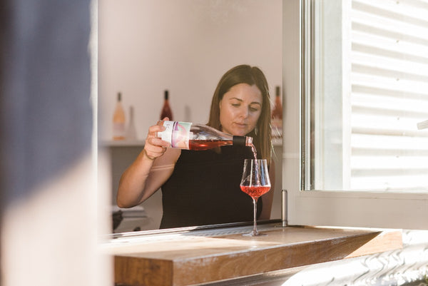 Woman pouring light red wine into glass on windowsill