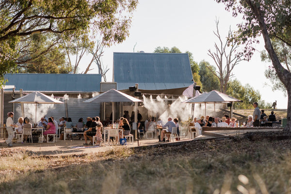 Crowd sitting under umbrellas next to winery shed