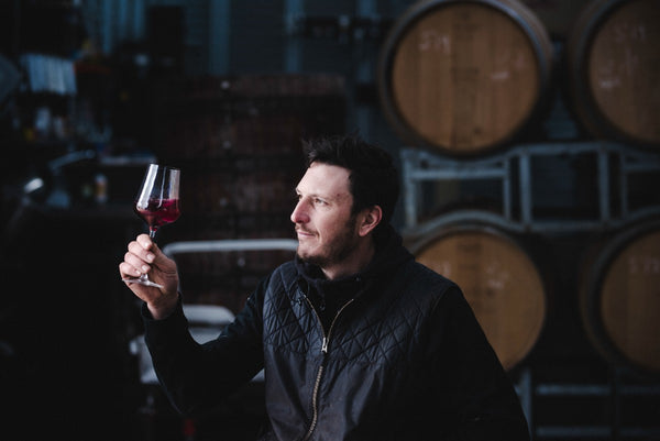 Man holding up a glass of wine in front of barrels