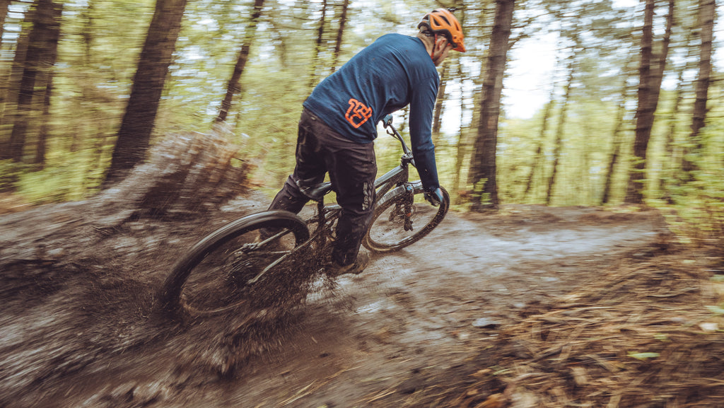 Mountain biker wearing a Broken Riders t-shirt and riding throuhg mud