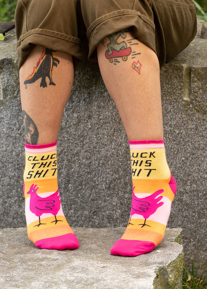 Ankle socks with a chicken and the words "Cluck This Shit" are worn with cuffed shorts
