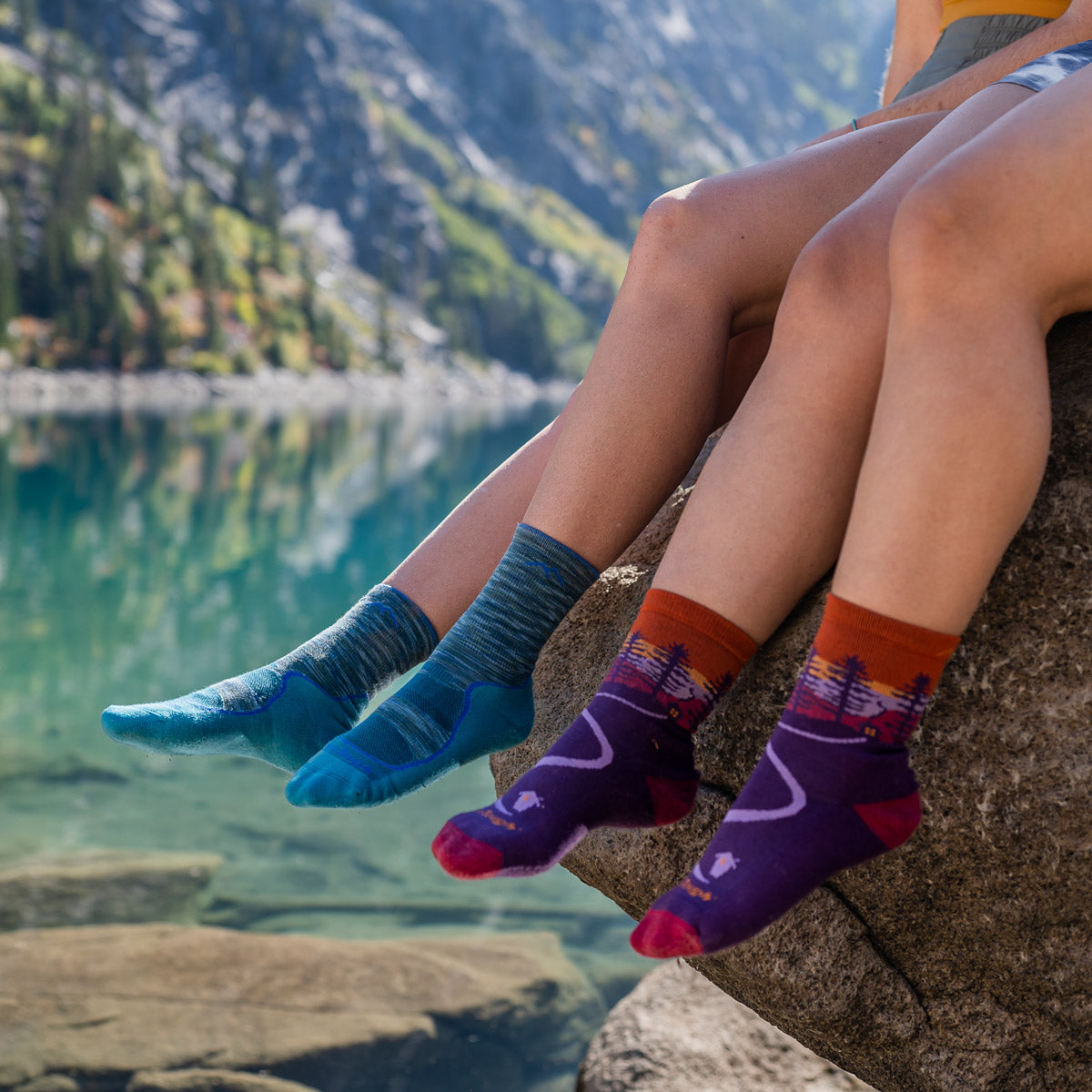 Two women wear Darn Tough socks in an outdoor setting beside a lake