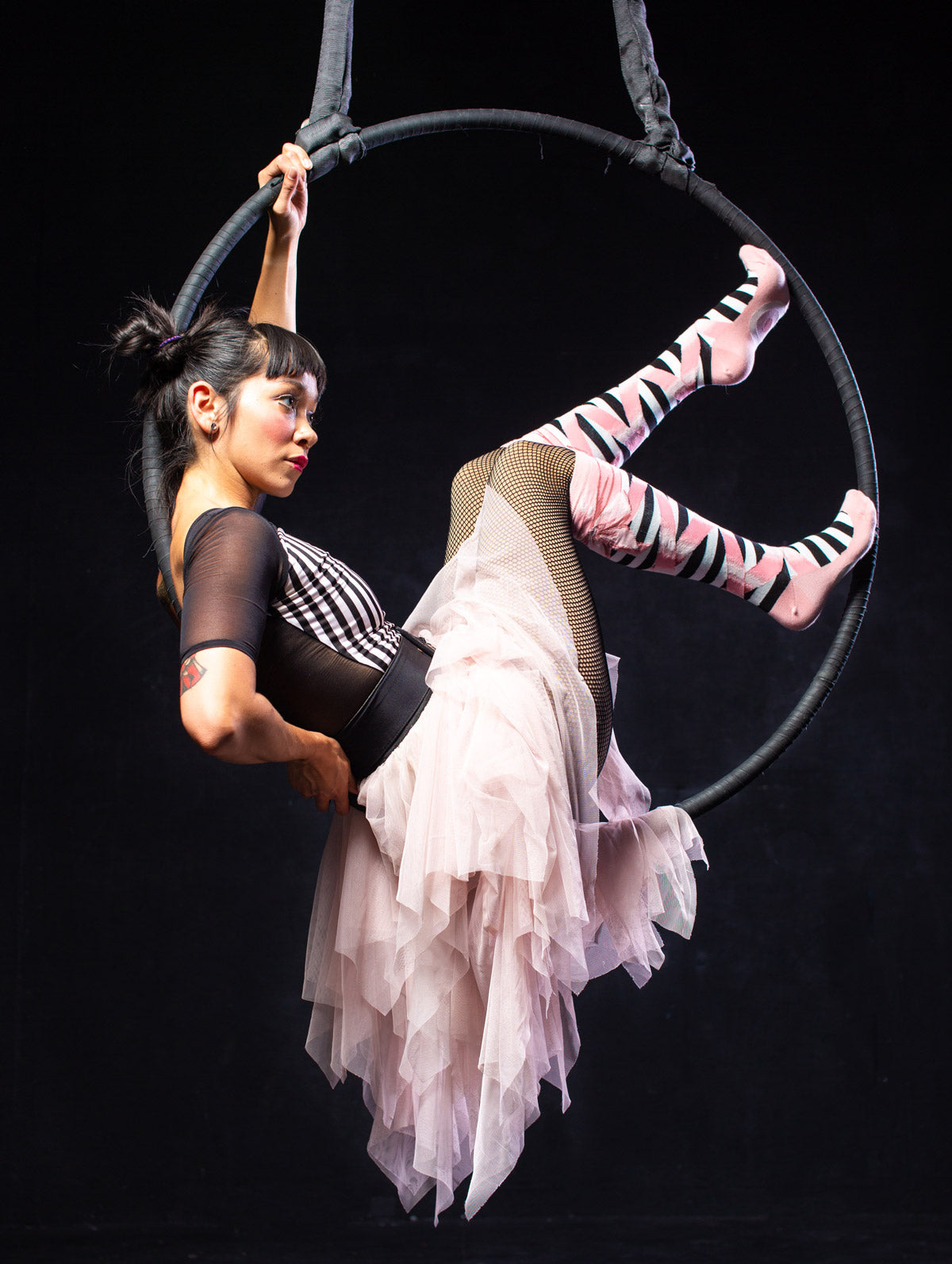 Aerial acrobat wears a tutu skirt with ballet slipper socks while sitting on an aerial hoop