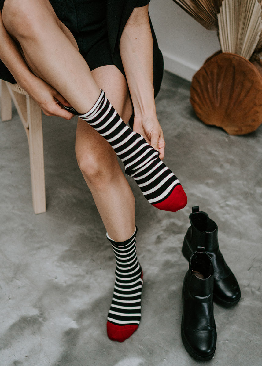 A person puts on a pair of striped bamboo socks with red toes