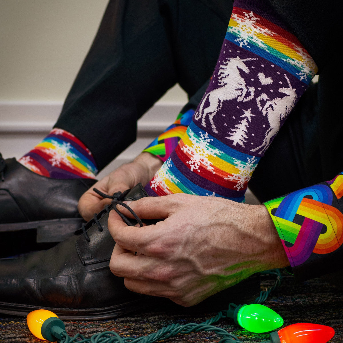 A person wears Gay Apparel Men's Christmas Socks and sits beside a string of Christmas lights