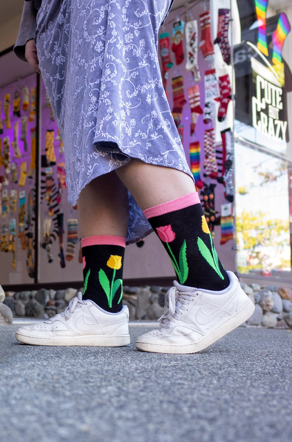 Hailey wears tulip crew socks with a purple skirt and white shoes at the entrance to Cute But Crazy Socks in Bellingham, Washington