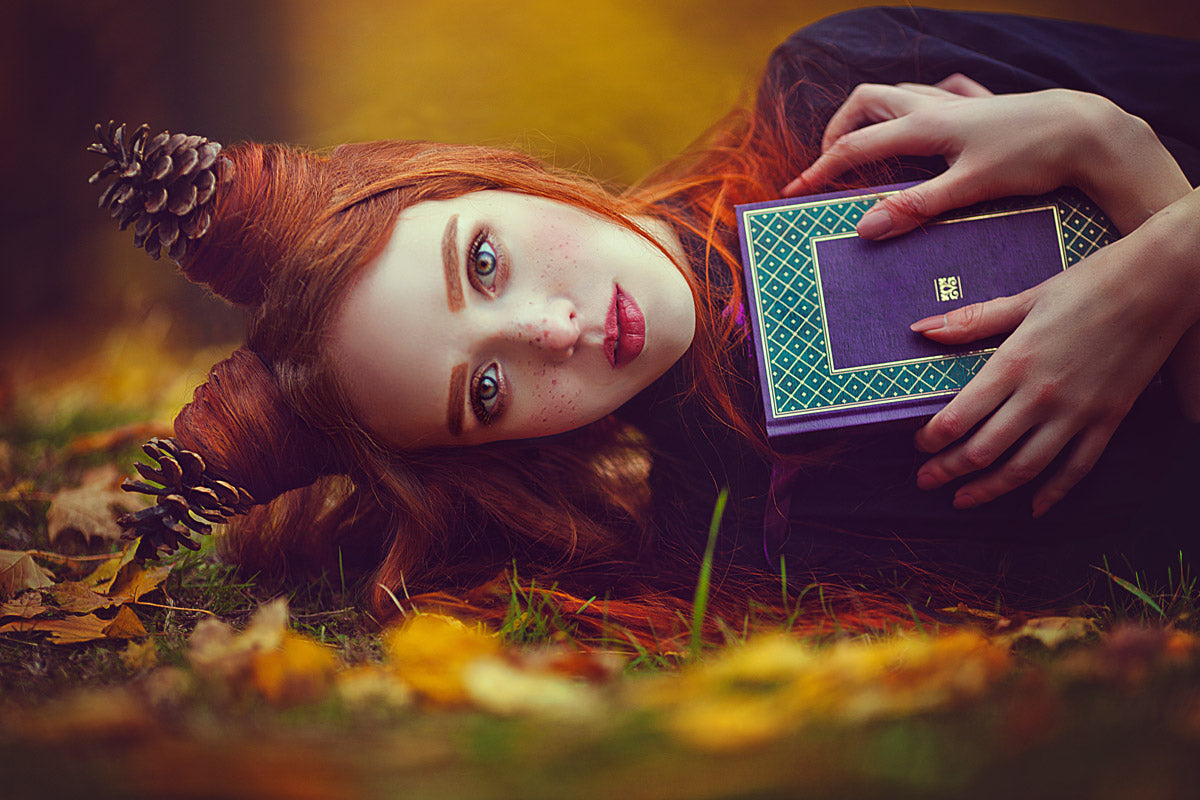 A woman lays on the ground holding a book with a fall pinecone hairstyle