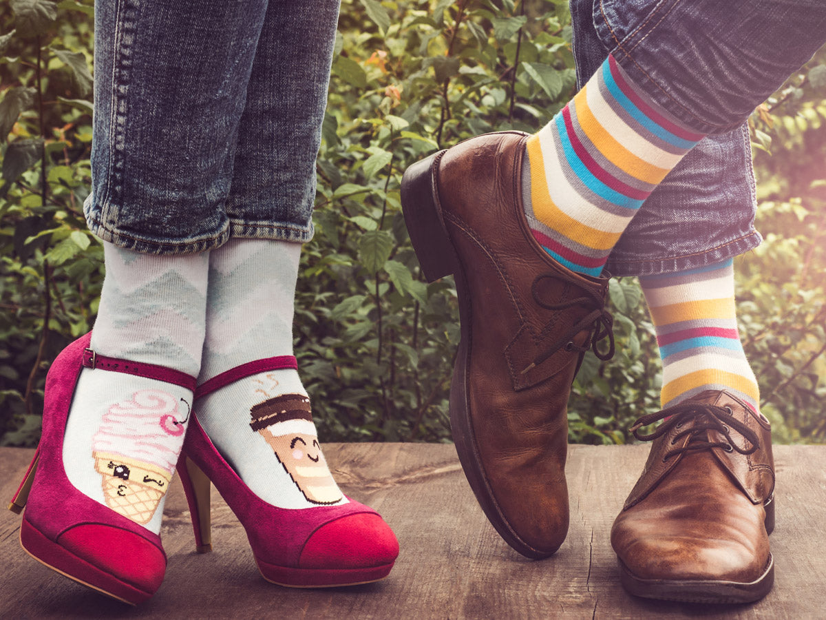 Feet in red heels and women's socks with coffee and ice cream stand beside feet in striped colorful socks andmen's dress shoes