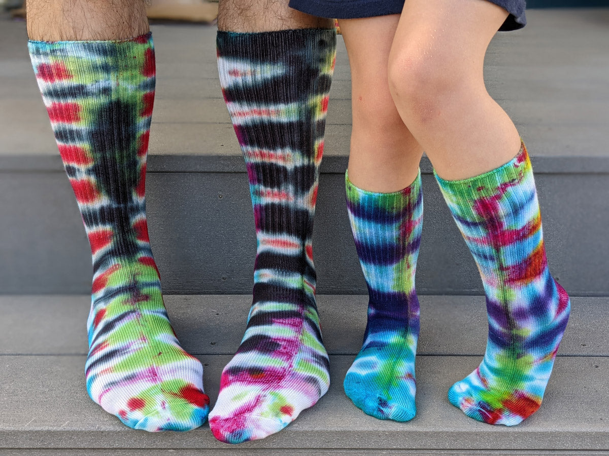 Finished tie-dye socks with bright colorful patterns are worn by a kid and parent who made them together.