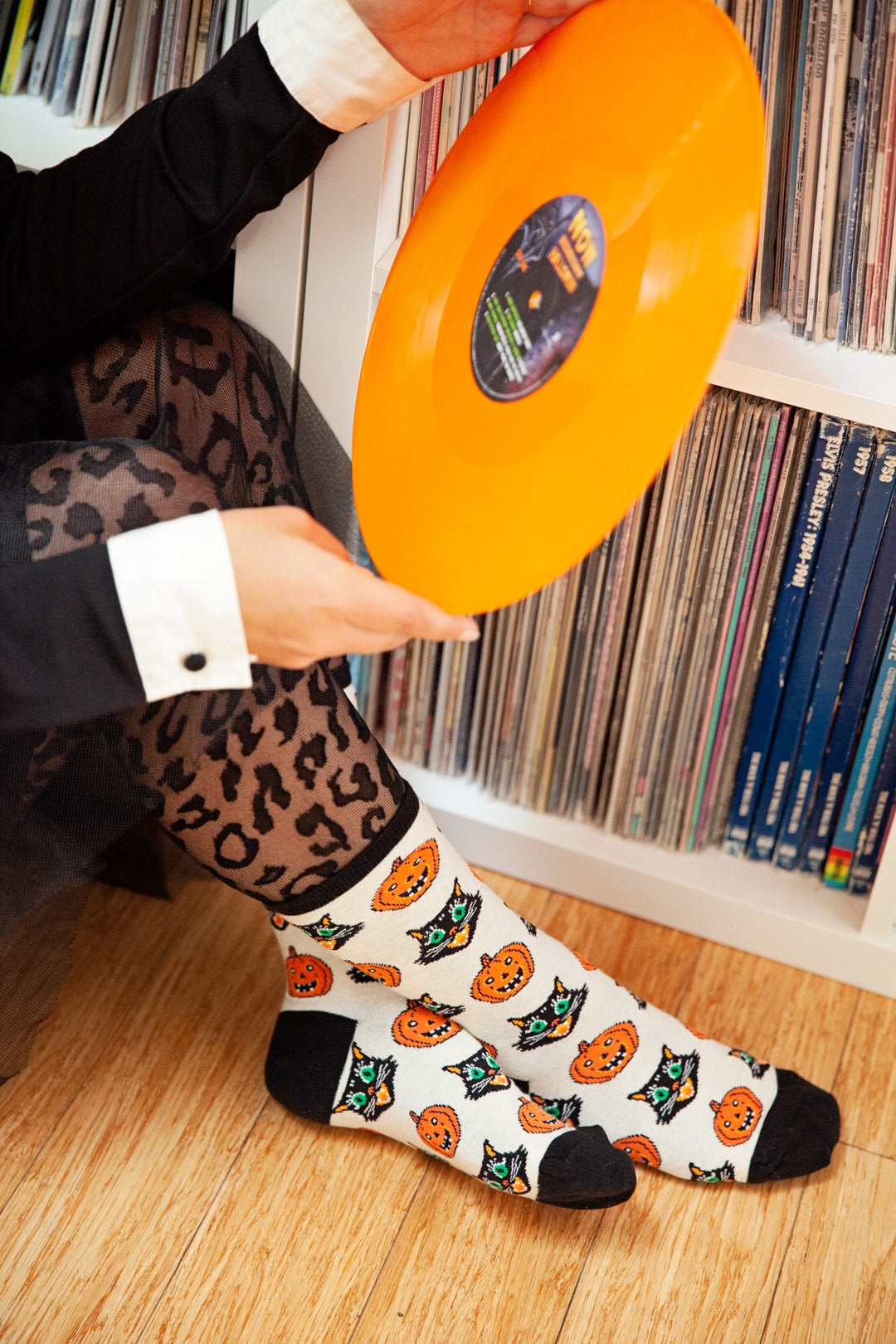 A fashionable person wears a black dress with white cuffs, black tights with a leopard print texture and vintage-inspired Halloween socks with retro cats and jack-o-lanterns