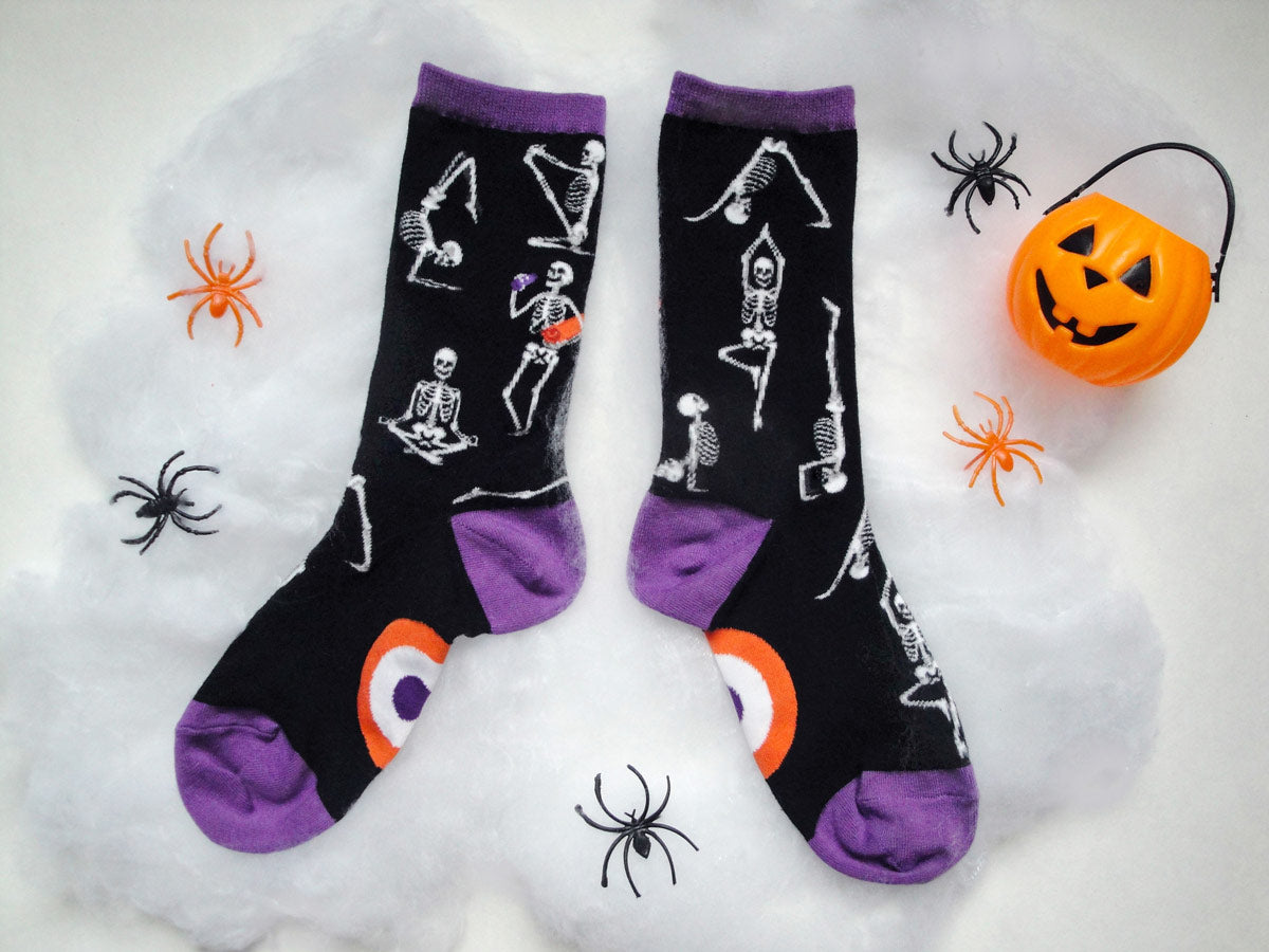 Skeleton socks with skeletons doing yoga lay on faux spiderwebs with black and orange plastic spiders.