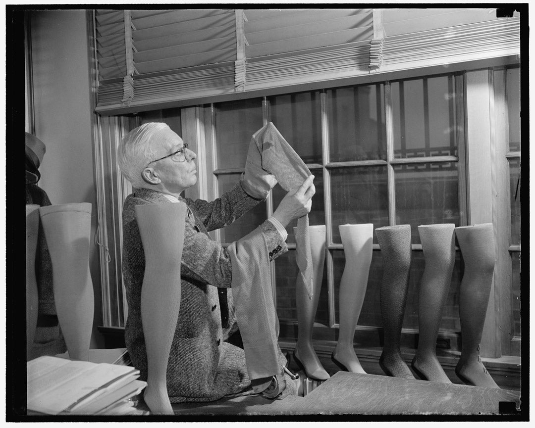 An man inspects a row of cotton stockings in a black and white photograph from 1941.