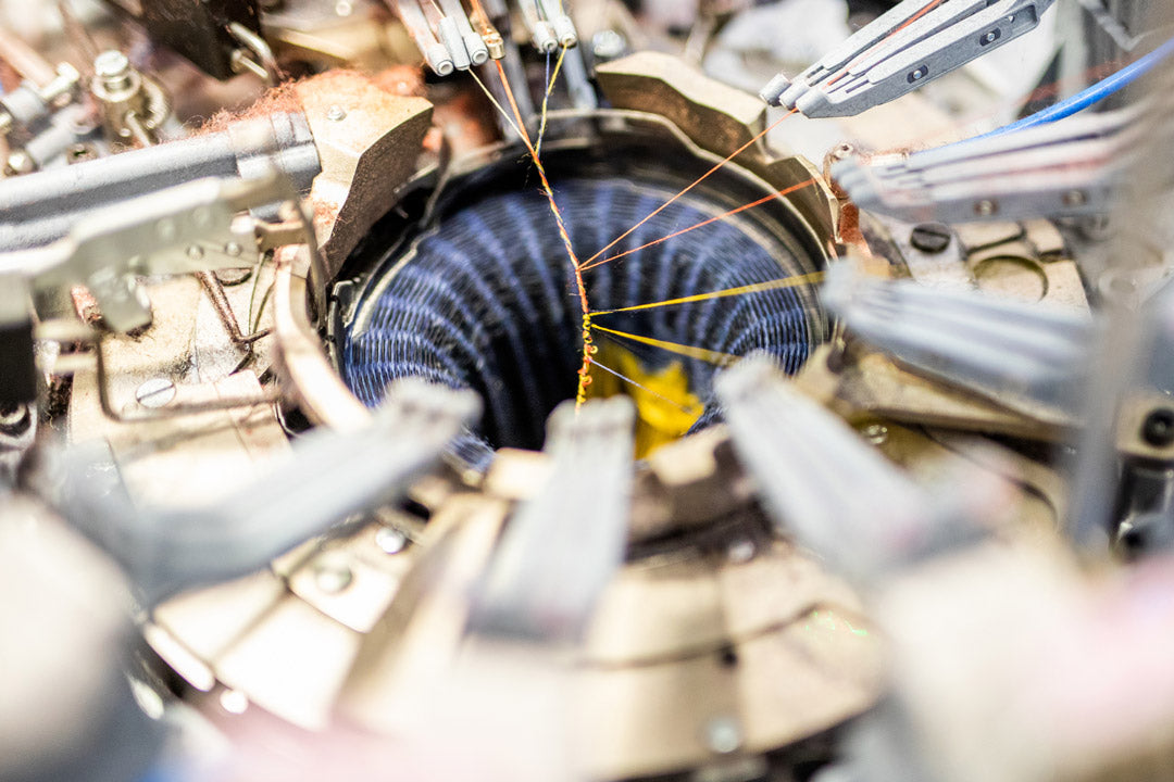 A modern circular knitting machine creates a sock from merino wool thread.