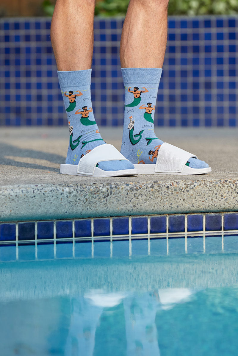Funny men's socks with mermen worn with flip-flops beside a pool.