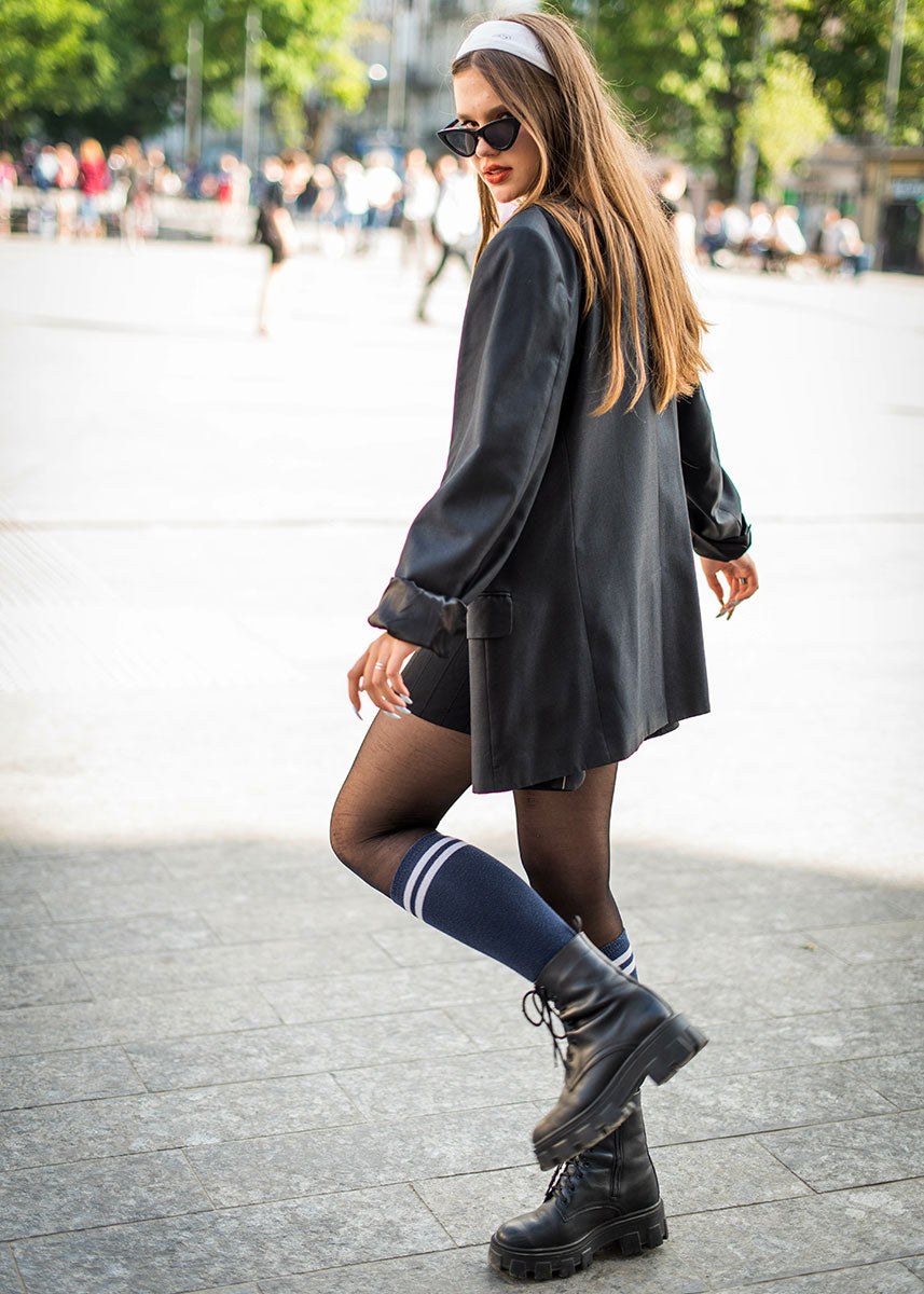 A woman wears an all-black outfit with knee socks, boots, shorts and a long shirt.