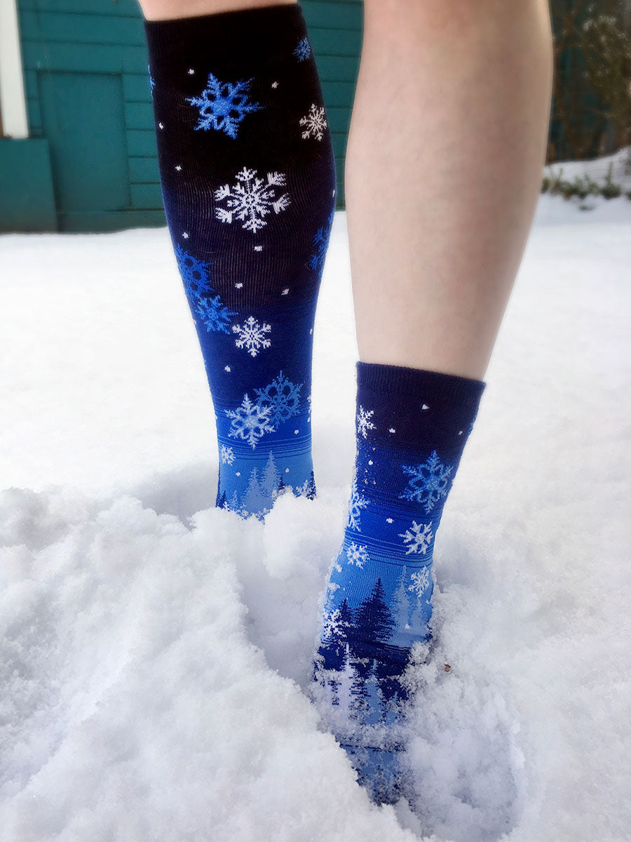 A person stands in the snow wearing socks with snowflakes and no shoes
