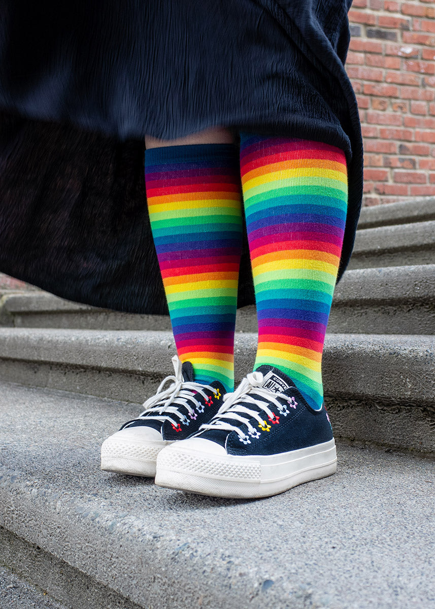 Hailey wears Rainbow Gradient knee socks with a black skirt and black Converse shoes