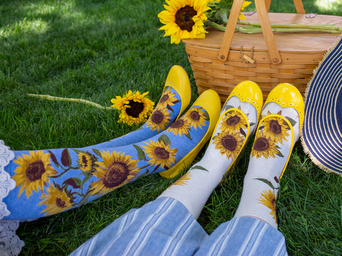 Two people wear sunflower socks and sit beside actual sunflowers