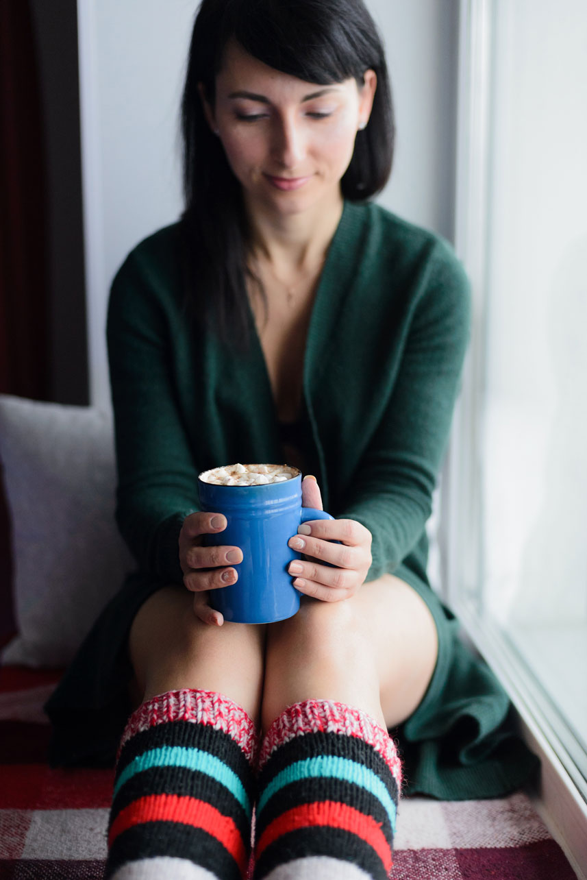 Cozy striped knee socks are worn by a woman in a sweater sitting indoors with a mug in her hands