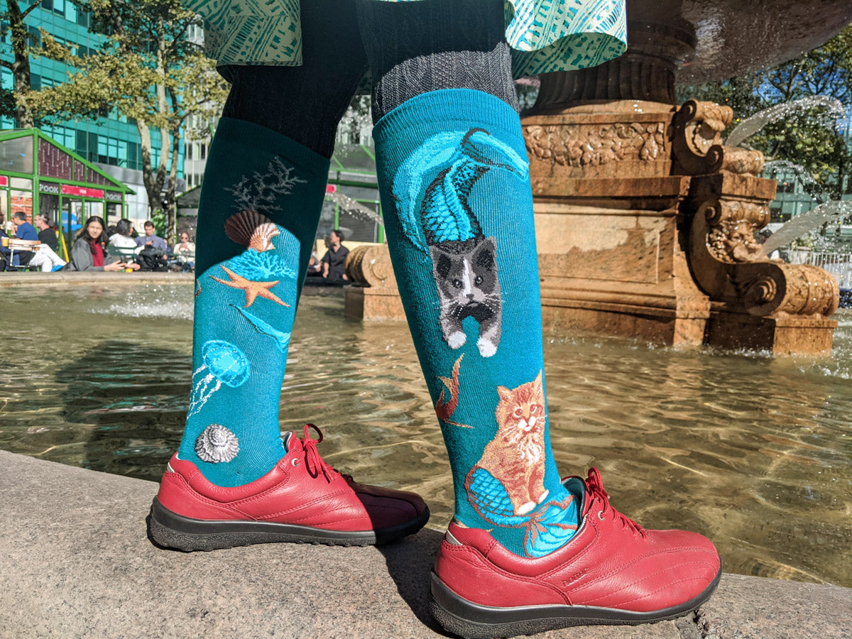 Purrmaids cat mermaid knee socks worn with red shoes and standing beside yet another fountain!