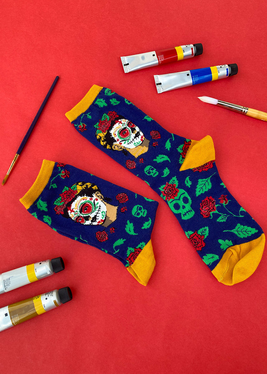Frida Kahlo art socks for Dia De Los Muertos pictured with paints and paintbrush