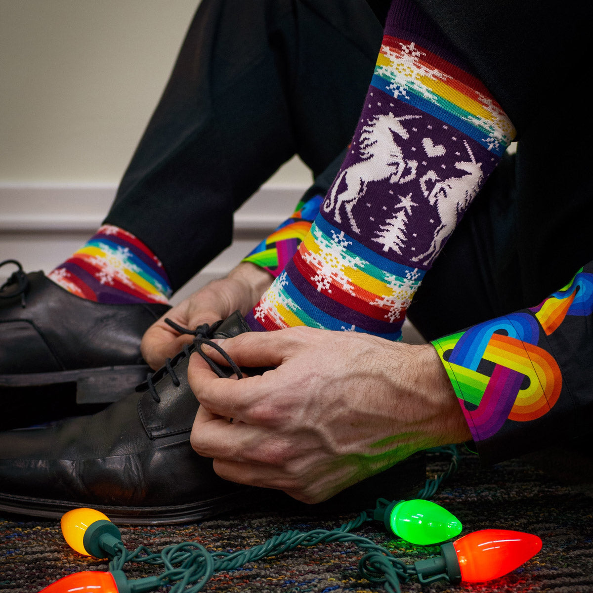 A man wears purple and rainbow Christmas socks that perfectly coordinate with his purple and rainbow shirt