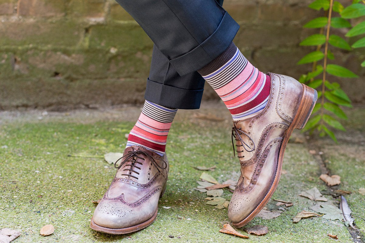 A man in brown shoes wear thin striped socks in primarily red, black and white tones