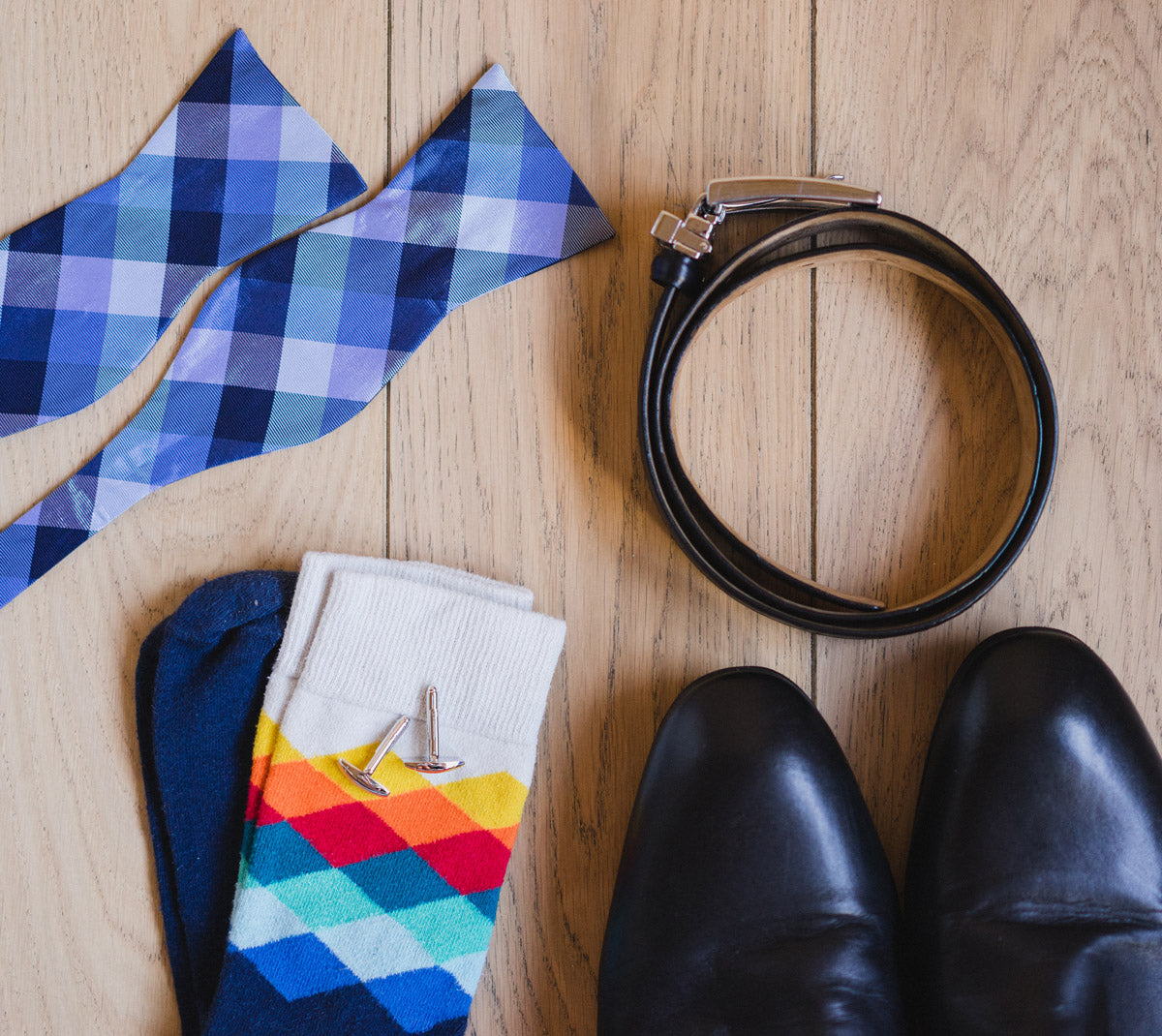 A layout of colorful socks a coordinated with a bold blue tie, black belt and black shoestie