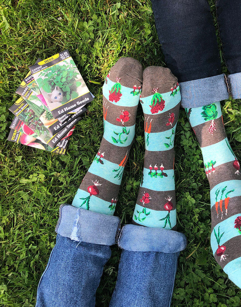 Vegetable garden socks lay on feet in grass beside a selection of seed packets