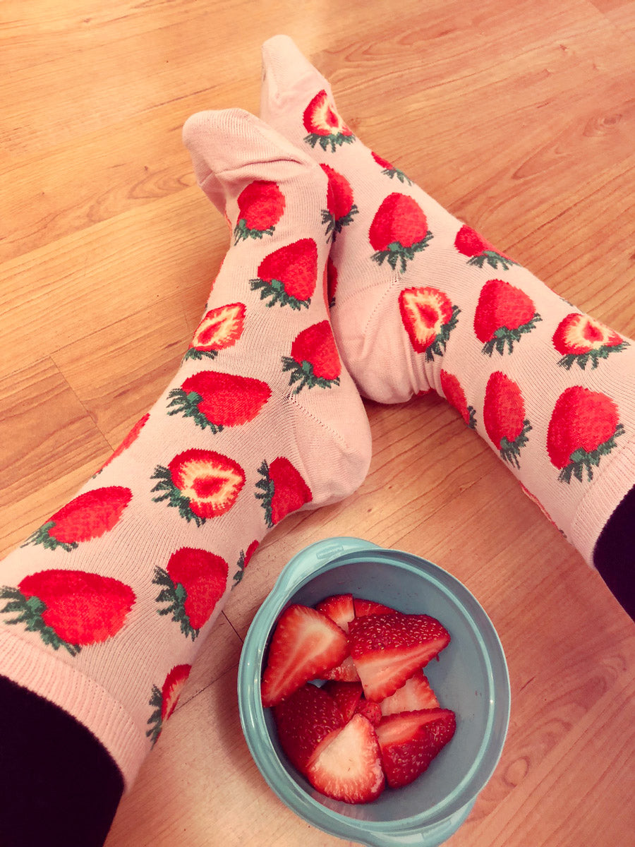 A model wears a pair of pink crew socks covered in bright red strawberries.