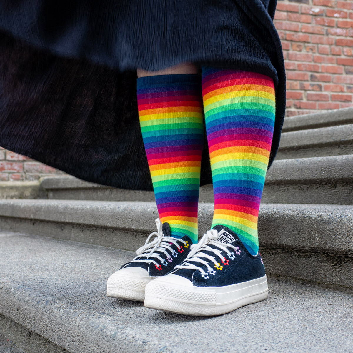 Rainbow gradient knee socks are worn with black and white Converse