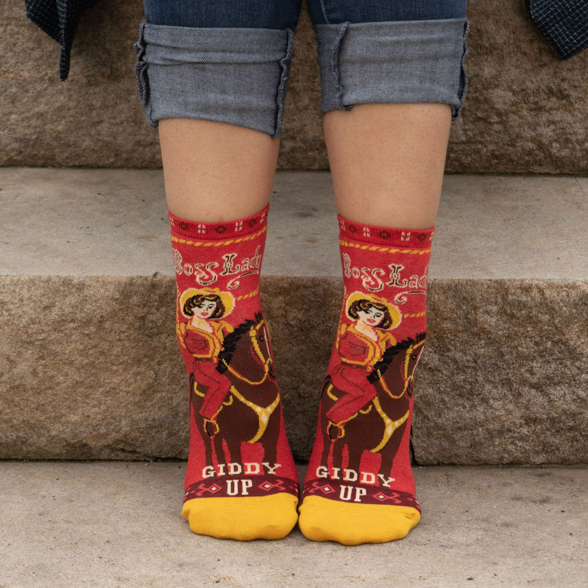 A person wears red socks with cowgirls riding horses and the words "Boss Lady"