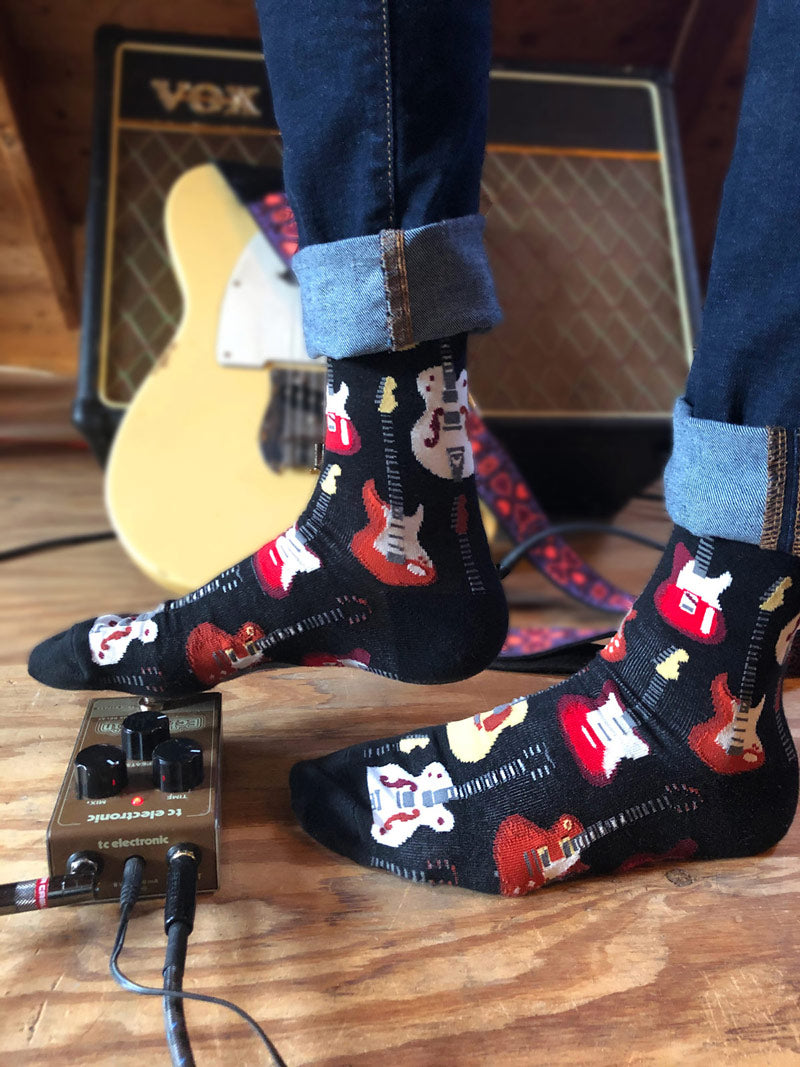 Guitar socks worn with cuffed jeans with amp and guitar in the background.