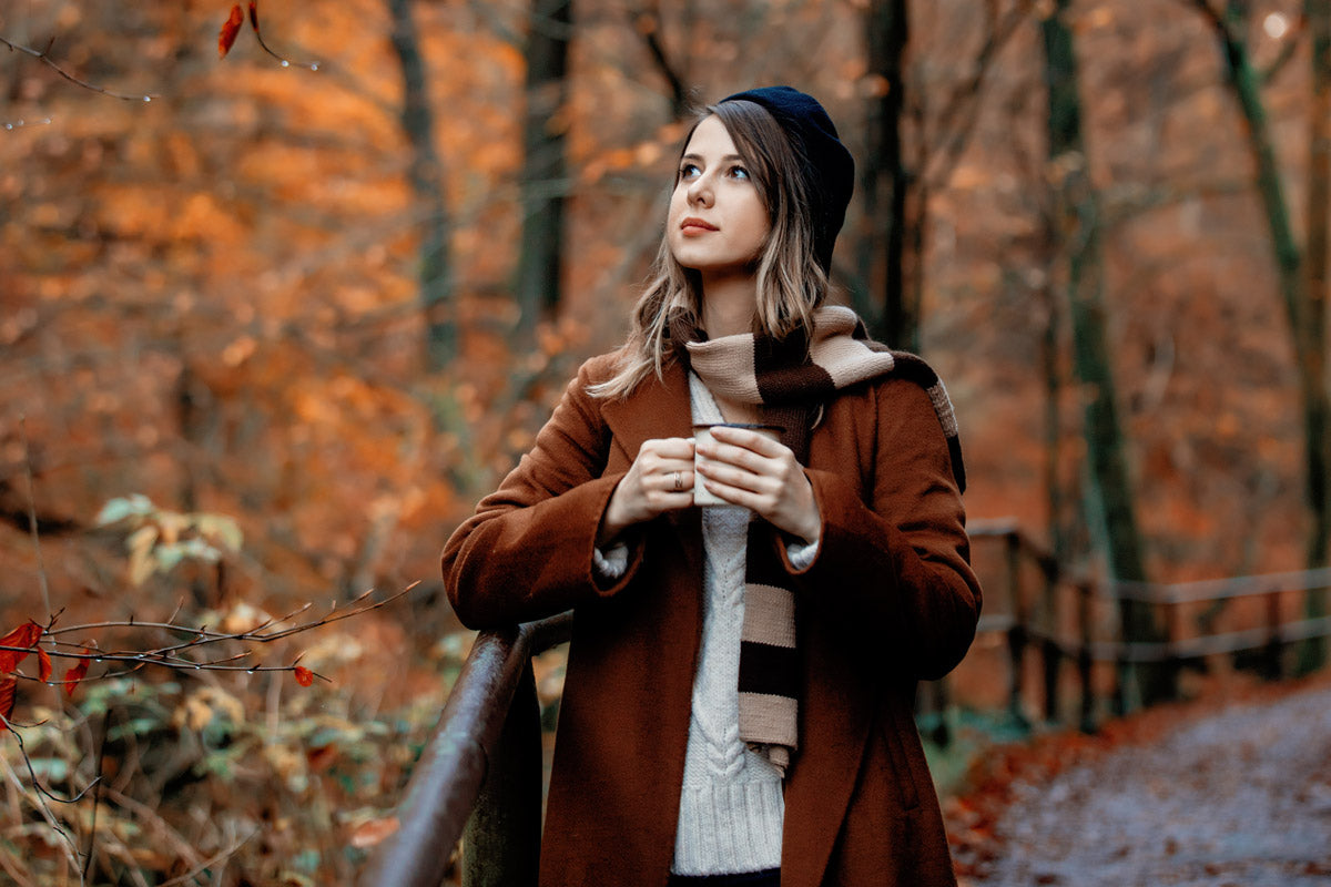A woman walks through a fall forest in a warm sweater, coat and hat