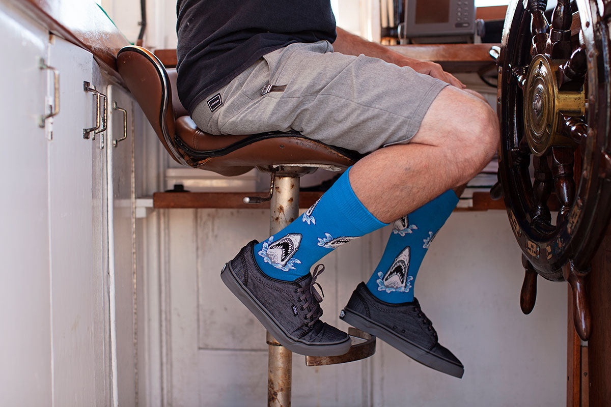 A man wears shorts and gray tennis shoes with blue shark socks