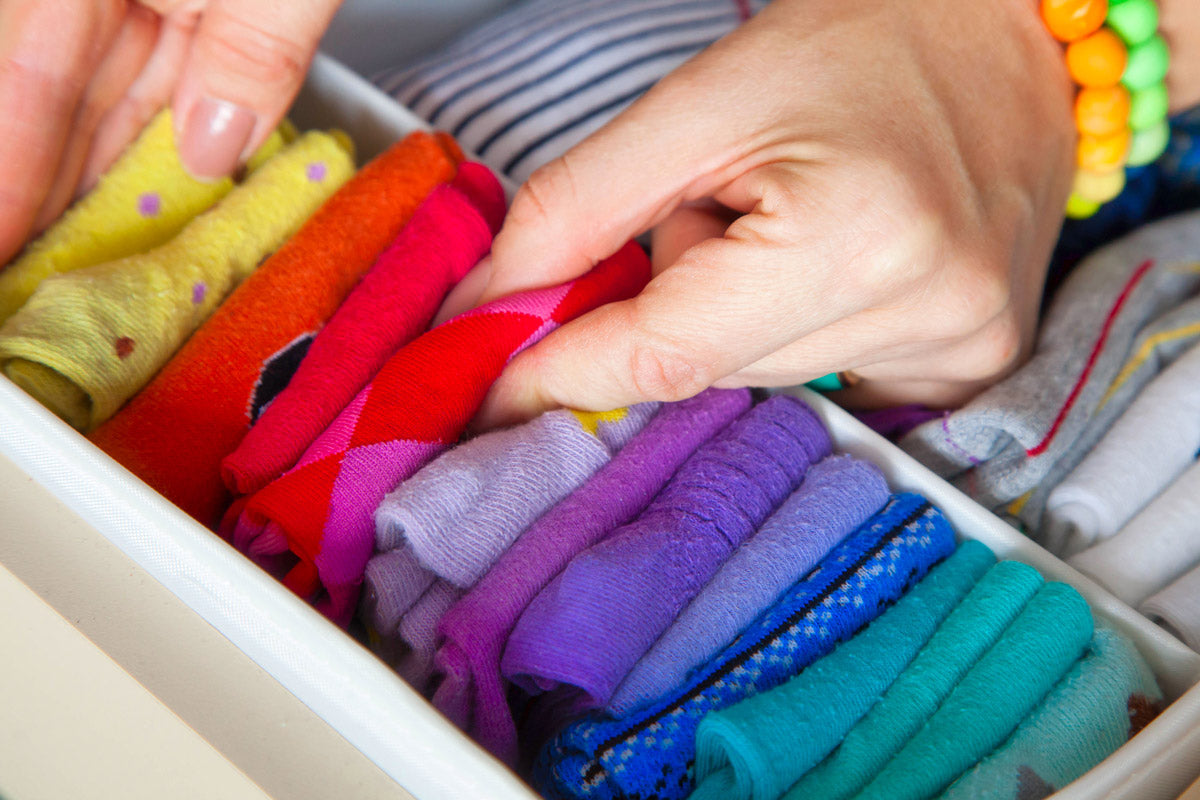 Hands arrange colorful socks folded in a sock drawer