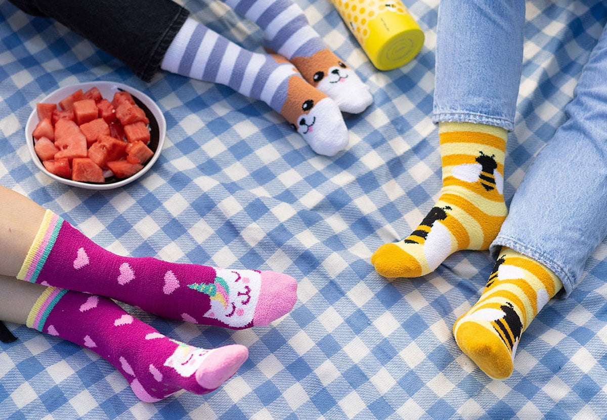 Three people sit on a picnic blanket, all wearing fuzzy socks with animals on them.