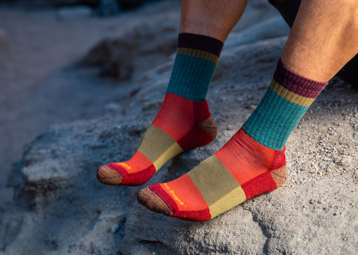 A person sits in a shadow on a rockface while wearing a pair of colorful Darn Tough hiking socks