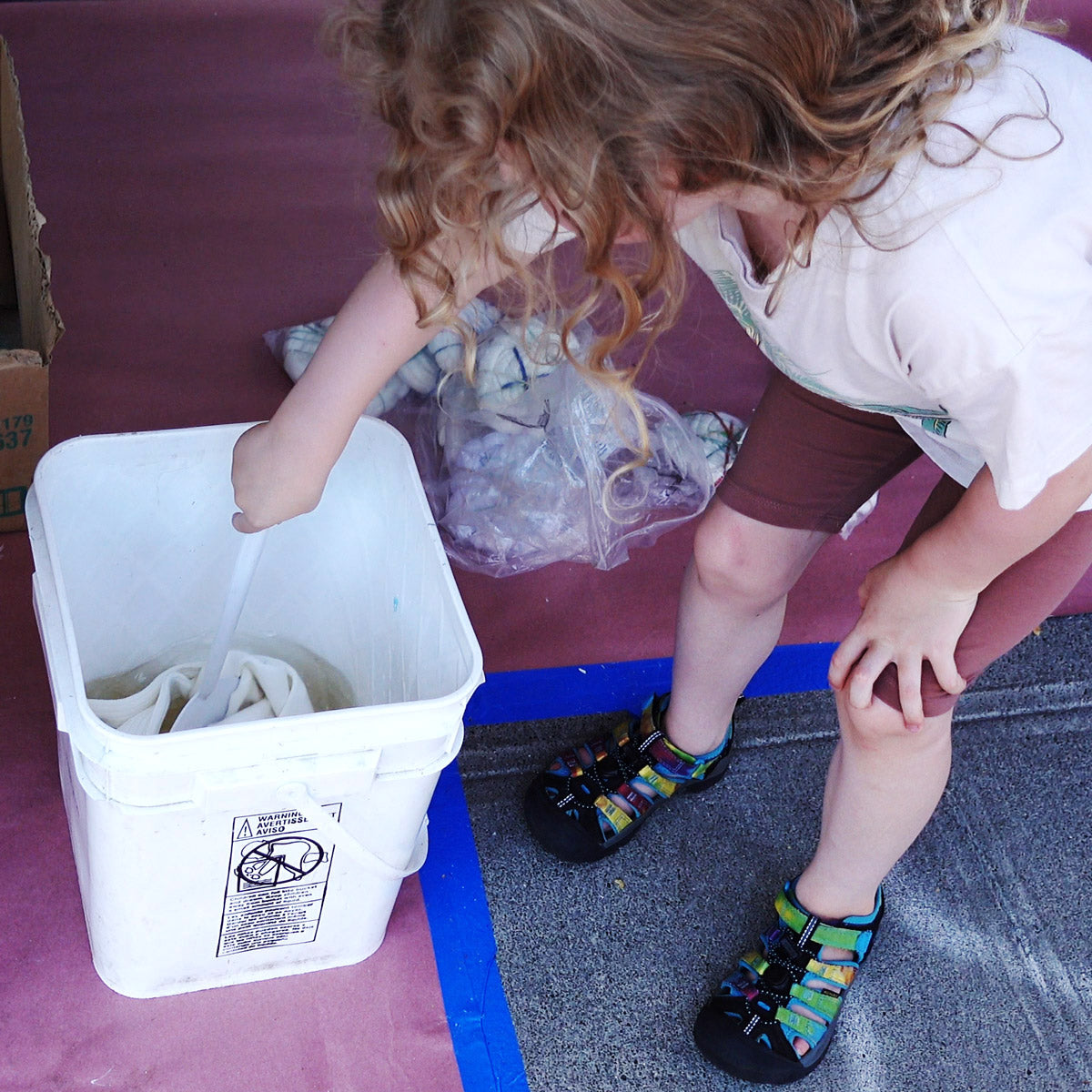 A child stirs socks soaking in the soda ash bucket to prepare them for tie-dye.