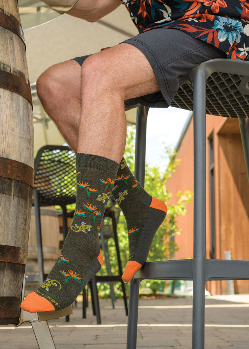 A man sits on a barstool wearing shorts and socks with a lizard and flower pattern