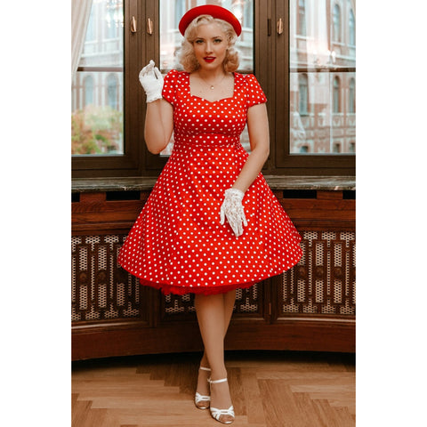 Vintage pinup style blonde model wearing a red and white polka dot fit and flare dress, white gloves and white high heels