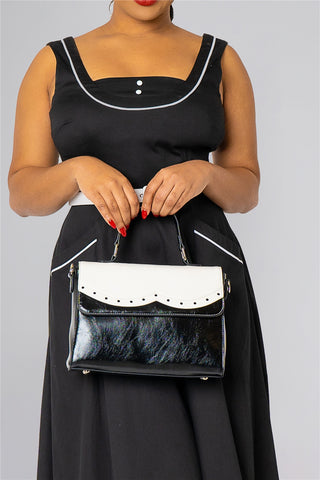 Woman in a black and white retro vintage dress holding a black and white handbag.