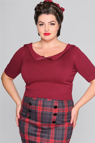 Curvy brunette model wearing her brown hair in an up-do with a hair flower, a burgundy top and a tartan pencil skirt