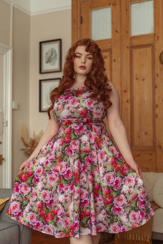 Sultry woman with long curly auburn hair wearing a pink floral 50s style fit and flare dress