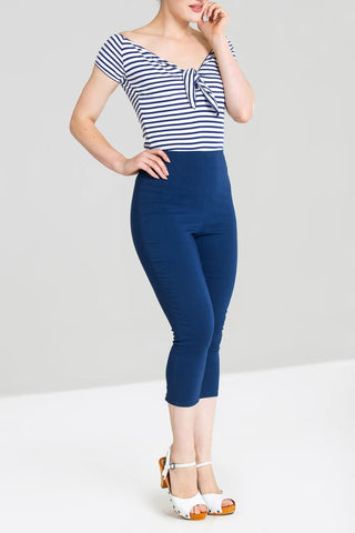 Young woman standing in navy blue capris and an off the shoulder blue and white striped top with white heeled shoes.