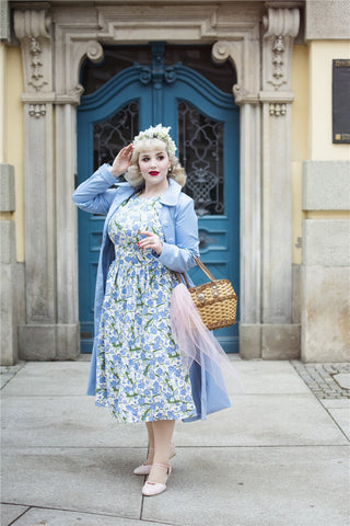 Glamorous blonde woman wearing a pastel blue floral dress and a long blue trench coat