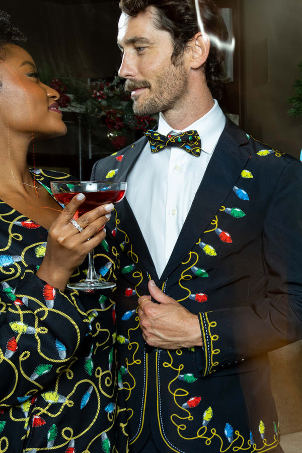 A man and woman in The Duke of December Christmas Lights Ugly Christmas Suit holding glasses of wine.